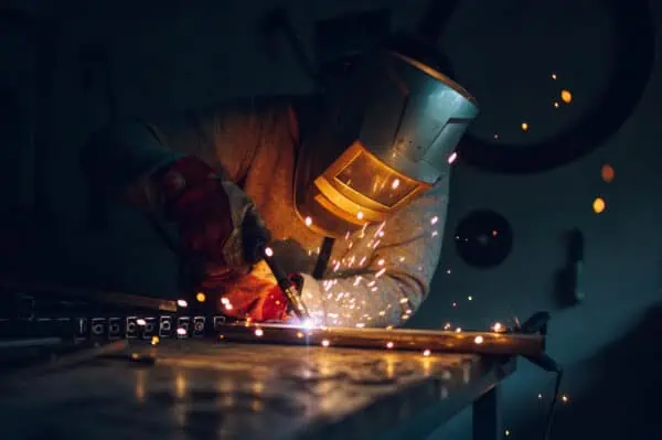 Welder working with a metal product and welding it with a arc welding machine in a workshop.